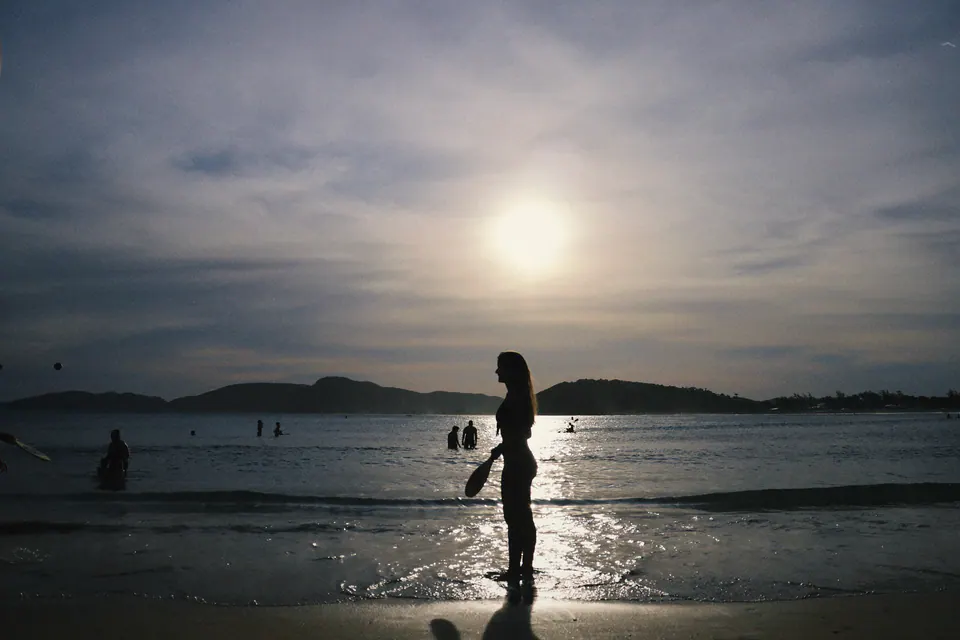 silhueta de mulher na beira do mar, com o sol entre as nuvens