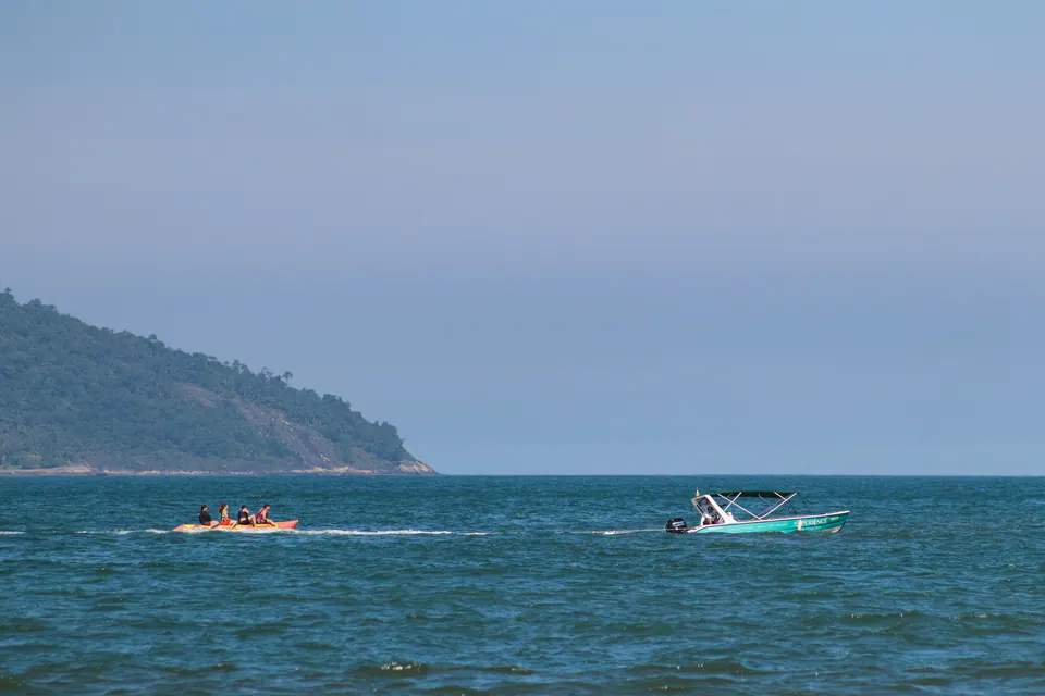 lancha cruza o mar azul perto de um morro verde