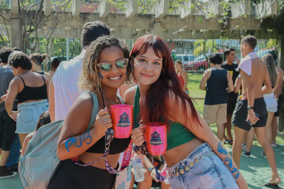 duas calouras sorriem para a câmera segurando canecas rosa da recepção